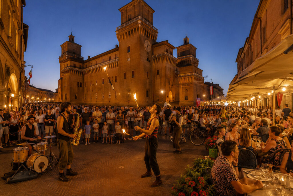Artisti di strada e pubblico durante il Ferrara Buskers Festival nel centro storico di Ferrara in una serata estiva.